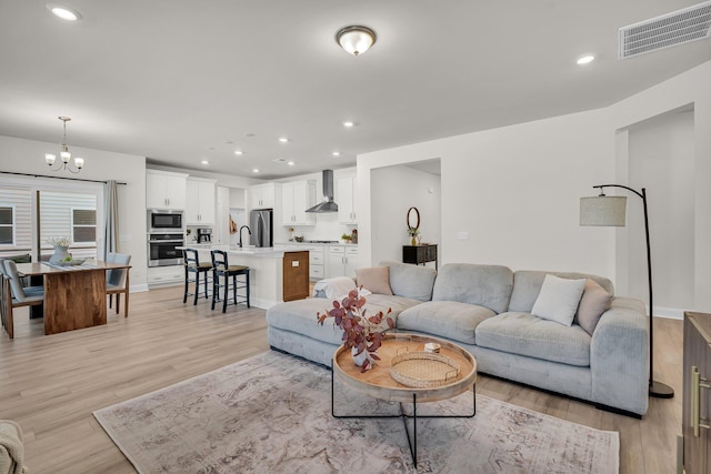 living room with sink, light hardwood / wood-style floors, and a chandelier