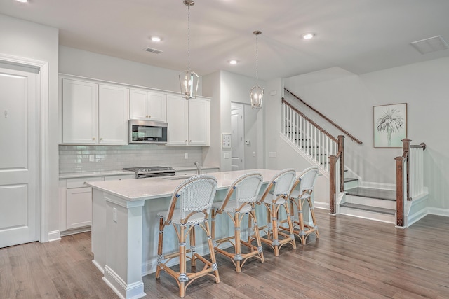 kitchen featuring white cabinetry, a center island with sink, a breakfast bar area, stainless steel appliances, and pendant lighting