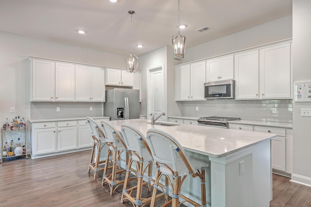 kitchen with pendant lighting, decorative backsplash, a kitchen island with sink, appliances with stainless steel finishes, and white cabinets