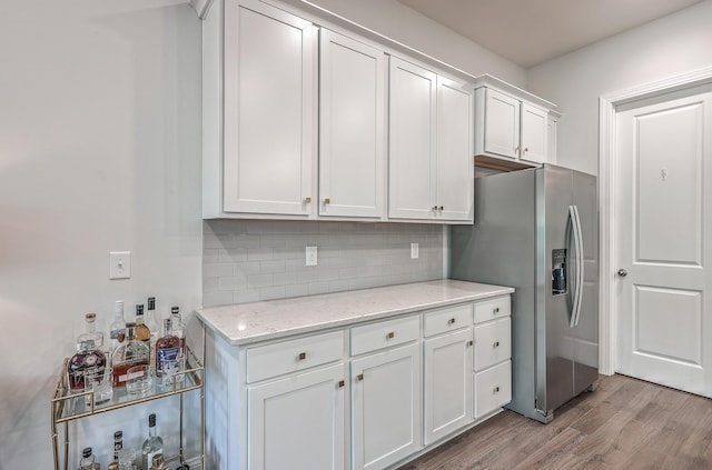 kitchen featuring white cabinetry, stainless steel fridge, decorative backsplash, light wood-type flooring, and light stone countertops