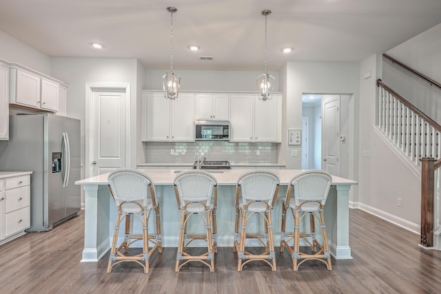 kitchen with decorative light fixtures, a kitchen bar, white cabinetry, stainless steel appliances, and a center island with sink