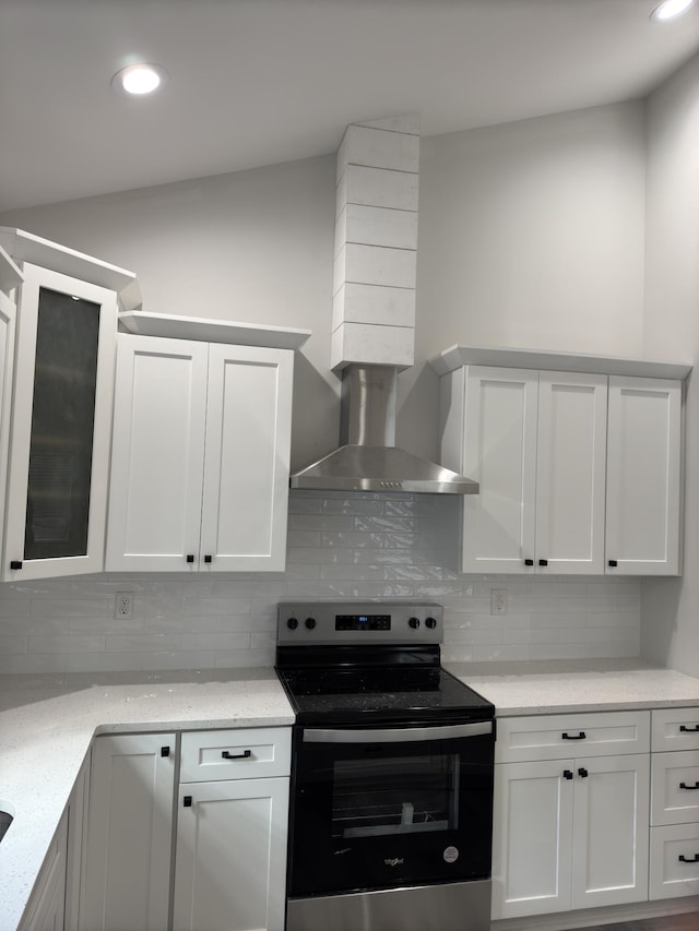 kitchen featuring light stone countertops, backsplash, wall chimney exhaust hood, stainless steel electric range oven, and white cabinetry