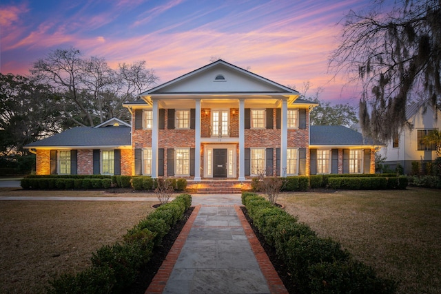 greek revival inspired property featuring a yard, covered porch, and brick siding