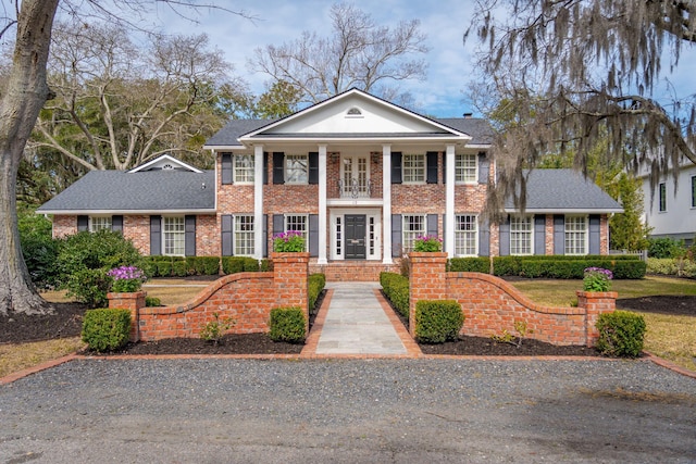 greek revival inspired property featuring french doors, brick siding, and a shingled roof