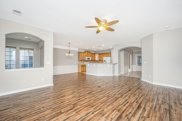 unfurnished living room featuring baseboards, visible vents, wood finished floors, and ceiling fan with notable chandelier