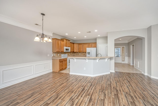 kitchen featuring tasteful backsplash, light countertops, light wood-style flooring, white appliances, and a kitchen breakfast bar