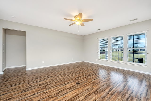 empty room with dark wood-style flooring, visible vents, and baseboards