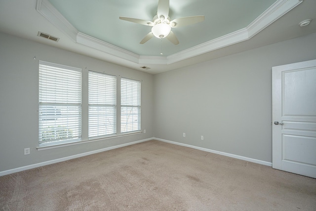 empty room featuring light carpet, baseboards, visible vents, a raised ceiling, and crown molding