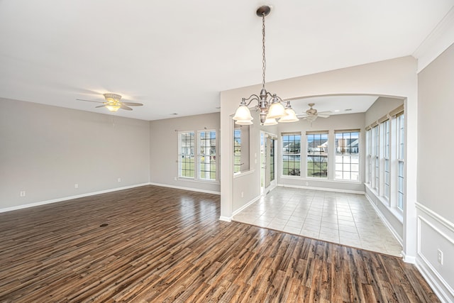 empty room featuring ceiling fan with notable chandelier, wood finished floors, a wealth of natural light, and baseboards