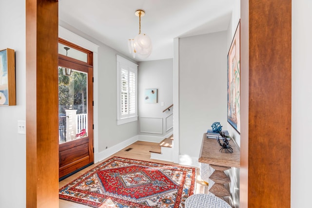 foyer with baseboards, visible vents, stairway, and wood finished floors