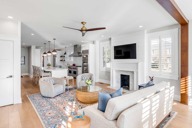 living area featuring a fireplace, light wood-style flooring, baseboards, and ceiling fan