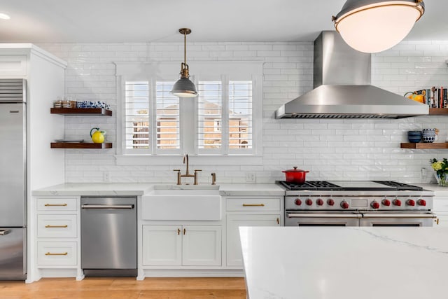 kitchen with a sink, high quality appliances, wall chimney range hood, light stone countertops, and open shelves