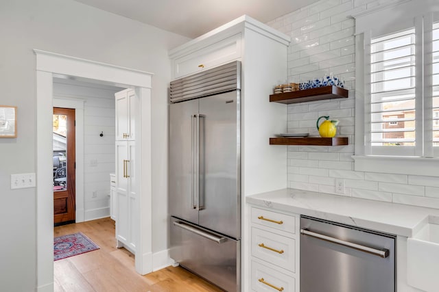 kitchen featuring white cabinets, light wood-style floors, stainless steel appliances, and decorative backsplash