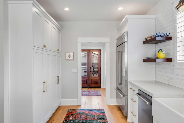 kitchen with stainless steel appliances, open shelves, white cabinetry, and light wood-style floors