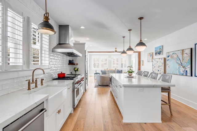 kitchen with a kitchen breakfast bar, appliances with stainless steel finishes, backsplash, wall chimney exhaust hood, and light wood finished floors