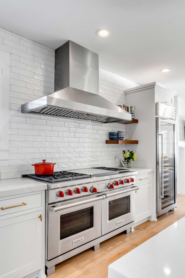 kitchen with premium appliances, wall chimney exhaust hood, light wood-style flooring, light countertops, and white cabinetry