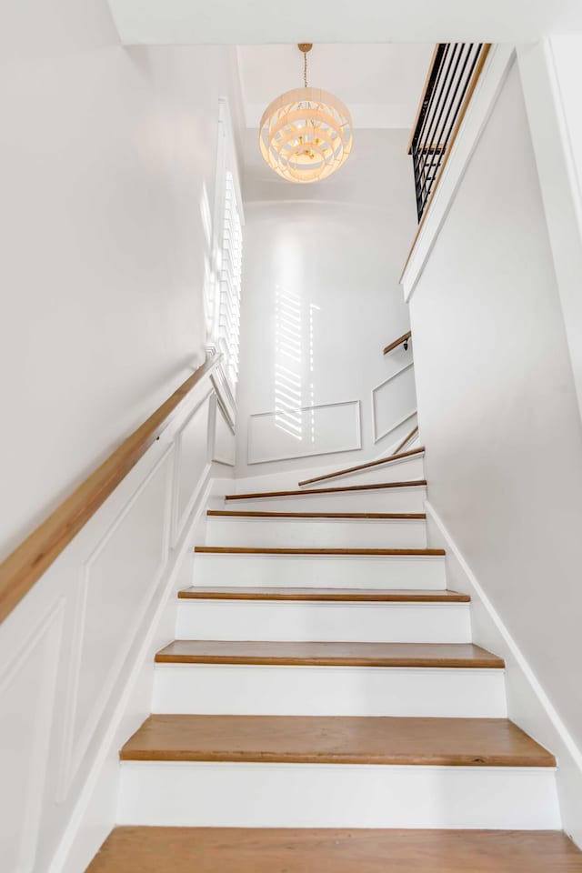 stairway with a chandelier, wainscoting, and a decorative wall