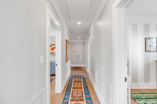 corridor featuring attic access, visible vents, light wood-style flooring, and baseboards