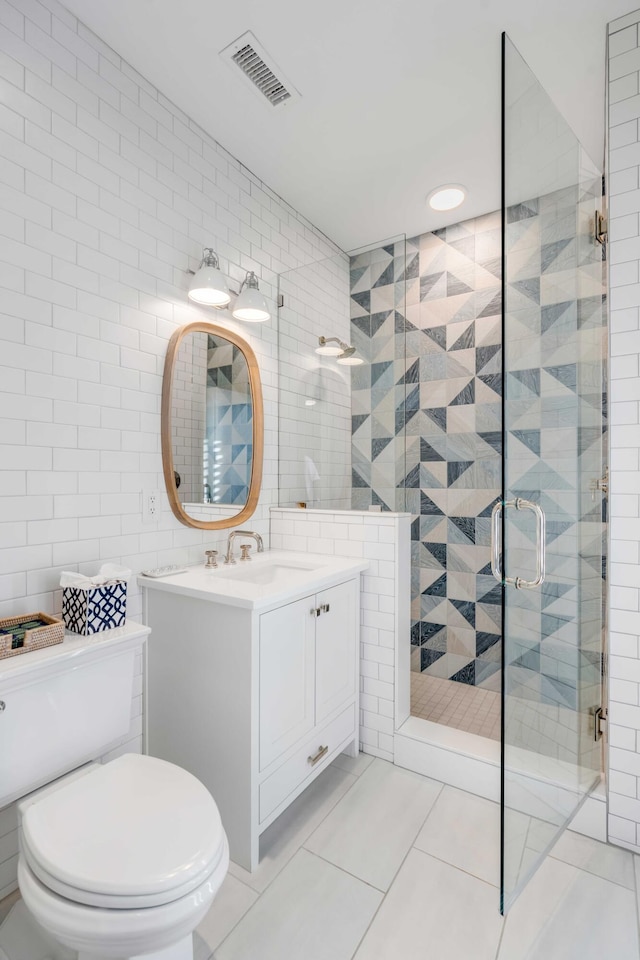 full bath with visible vents, toilet, vanity, a shower stall, and tile walls