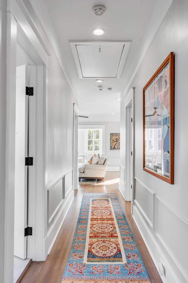 corridor featuring attic access, crown molding, a decorative wall, and wood finished floors