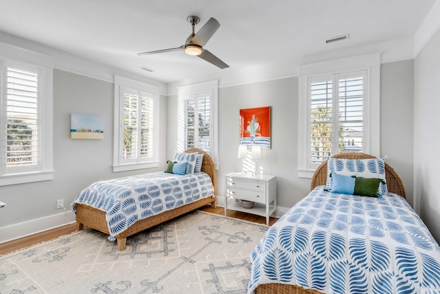 bedroom with a ceiling fan, visible vents, baseboards, and wood finished floors