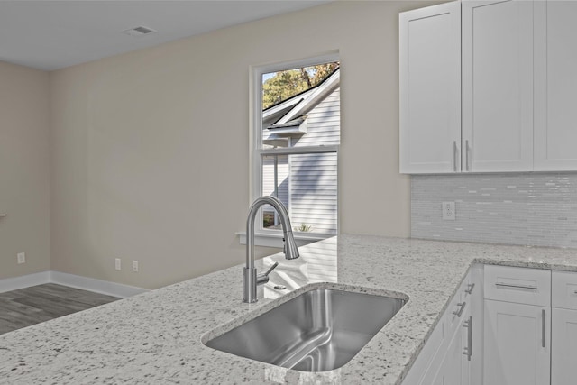 kitchen featuring hardwood / wood-style flooring, backsplash, sink, white cabinets, and light stone counters