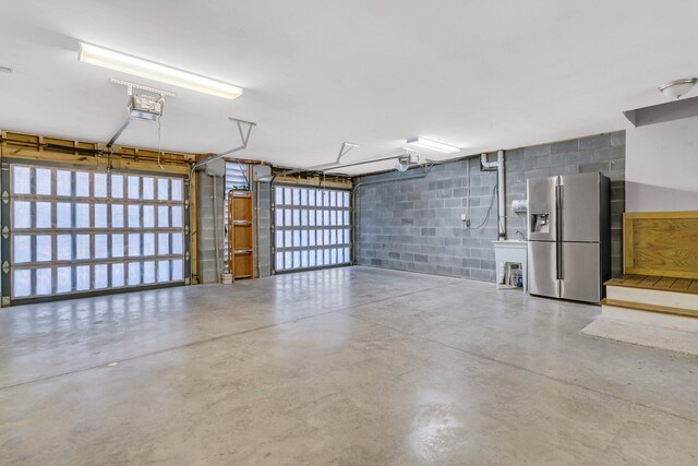 garage with a garage door opener and stainless steel refrigerator with ice dispenser