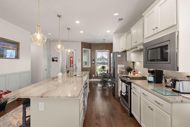 kitchen with hanging light fixtures, stainless steel appliances, an island with sink, white cabinets, and sink