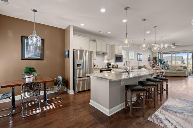 kitchen with hanging light fixtures, a kitchen bar, a large island with sink, white cabinets, and appliances with stainless steel finishes