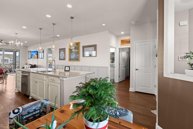 kitchen with light stone countertops, dark wood-type flooring, decorative light fixtures, a center island with sink, and sink