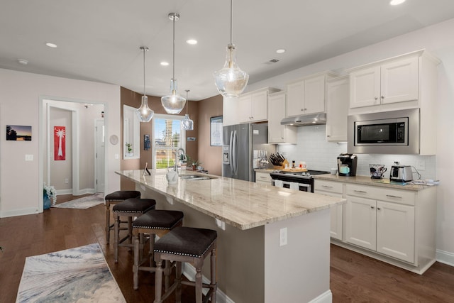 kitchen with white cabinets, appliances with stainless steel finishes, a kitchen island with sink, and hanging light fixtures