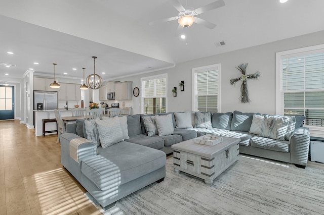 living room featuring ceiling fan with notable chandelier, light wood-type flooring, lofted ceiling, and ornamental molding