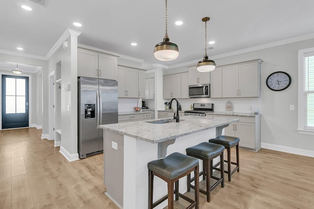 kitchen featuring a kitchen island with sink, stainless steel appliances, light stone countertops, sink, and a kitchen bar