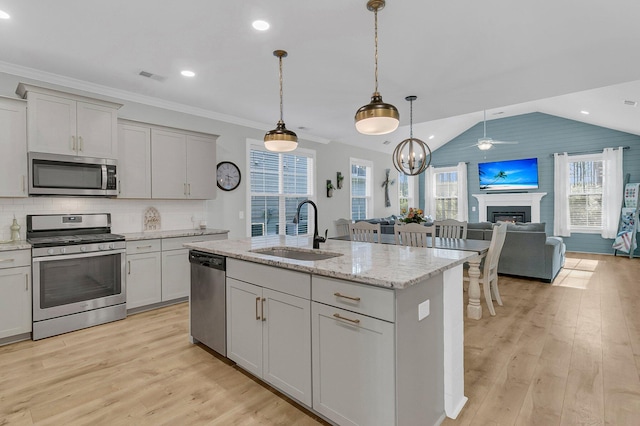kitchen featuring appliances with stainless steel finishes, sink, light stone counters, hanging light fixtures, and a kitchen island with sink