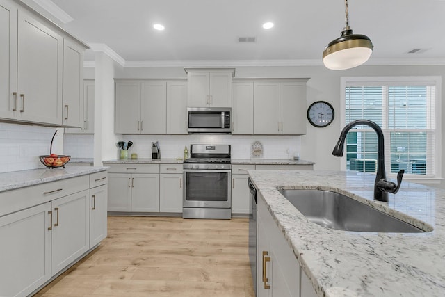 kitchen with light wood-type flooring, stainless steel appliances, sink, crown molding, and pendant lighting