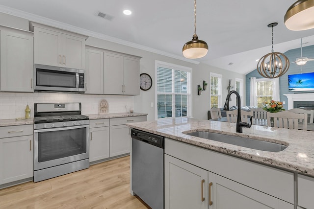 kitchen with decorative light fixtures, stainless steel appliances, light stone counters, and sink