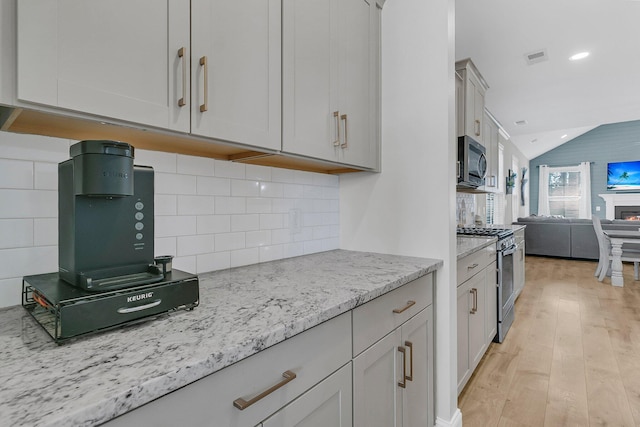 kitchen with appliances with stainless steel finishes, vaulted ceiling, light hardwood / wood-style flooring, light stone countertops, and decorative backsplash