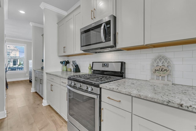 kitchen with ornamental molding, stainless steel appliances, white cabinets, and light stone counters