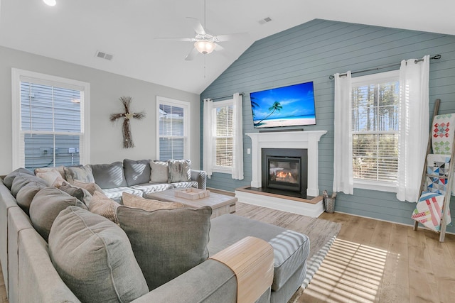 living room featuring light hardwood / wood-style floors, lofted ceiling, ceiling fan, and wooden walls