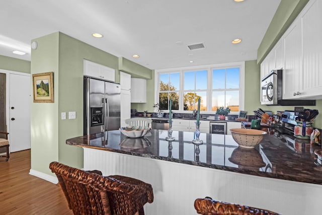 kitchen featuring hardwood / wood-style floors, white cabinetry, dark stone counters, kitchen peninsula, and stainless steel appliances