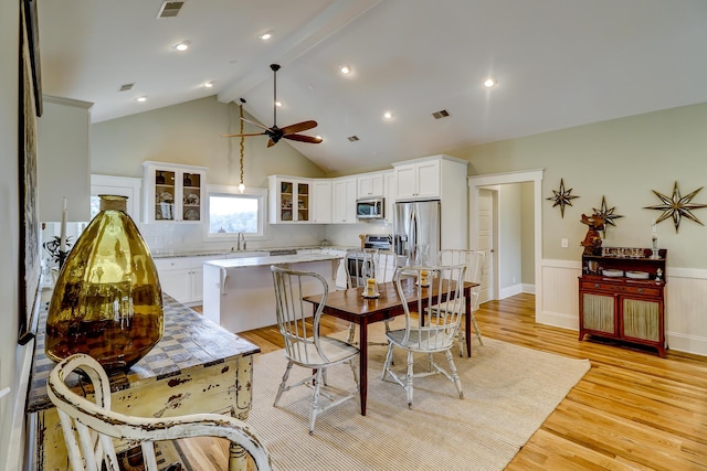 kitchen with visible vents, glass insert cabinets, beamed ceiling, wainscoting, and appliances with stainless steel finishes