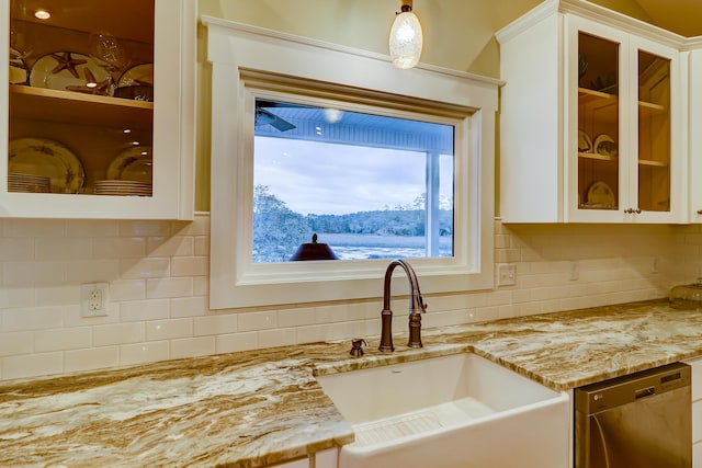 kitchen with glass insert cabinets, light stone countertops, dishwashing machine, white cabinets, and a sink