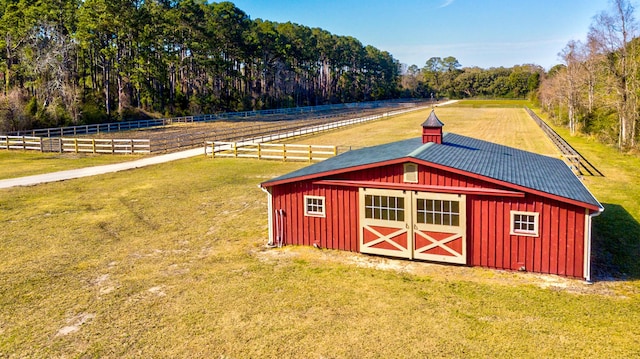 view of barn featuring a yard, a rural view, a wooded view, and fence