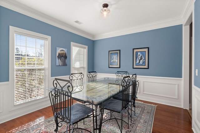 dining room featuring visible vents, ornamental molding, a wainscoted wall, and wood finished floors