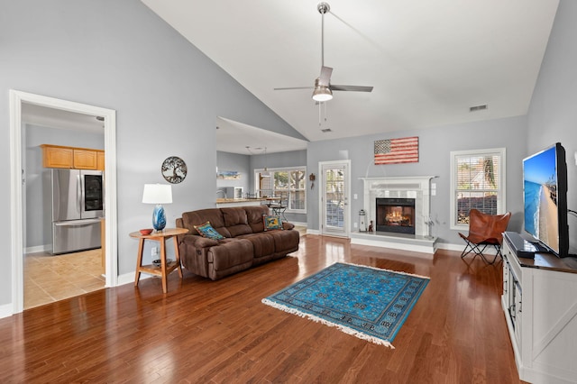 living room featuring light wood-type flooring, visible vents, high vaulted ceiling, a fireplace, and ceiling fan