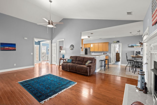 living room featuring visible vents, baseboards, light wood-type flooring, a fireplace, and a ceiling fan