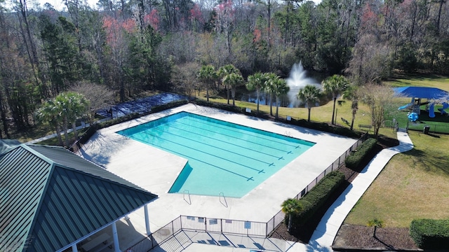 community pool with a yard, a view of trees, and a patio area