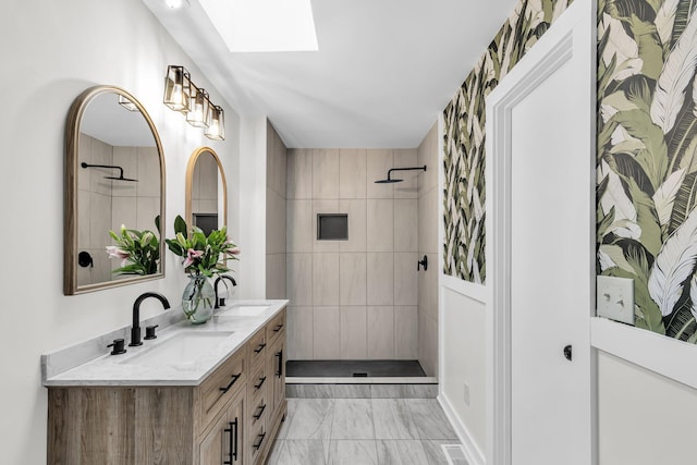 full bathroom with double vanity, a tile shower, a skylight, marble finish floor, and a sink