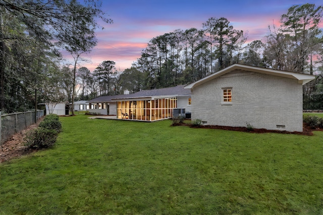 back of house at dusk with crawl space, fence, brick siding, and a sunroom