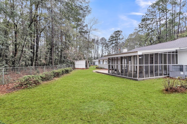 view of yard with an outbuilding, a fenced backyard, a shed, and a sunroom